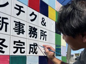 事務所完成告知看板。「成」の字の最後の点を、だるまの目のように入れるカワウチケンチク代表。